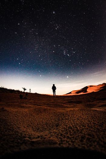 Silhouette person standing on desert against sky at night