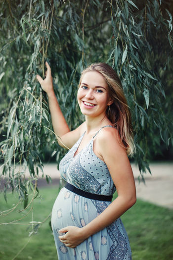 Portrait of pregnant woman touching abdomen while standing on grass