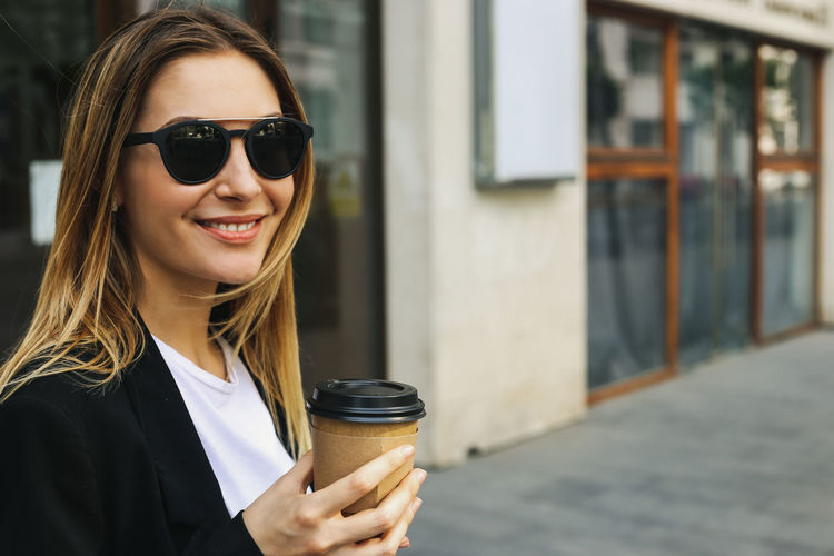 Portrait of woman holding sunglasses in city