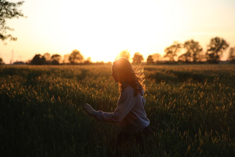 Young woman running in field at sunset