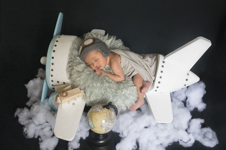 High angle view of baby sleeping over toy airplane against black background
