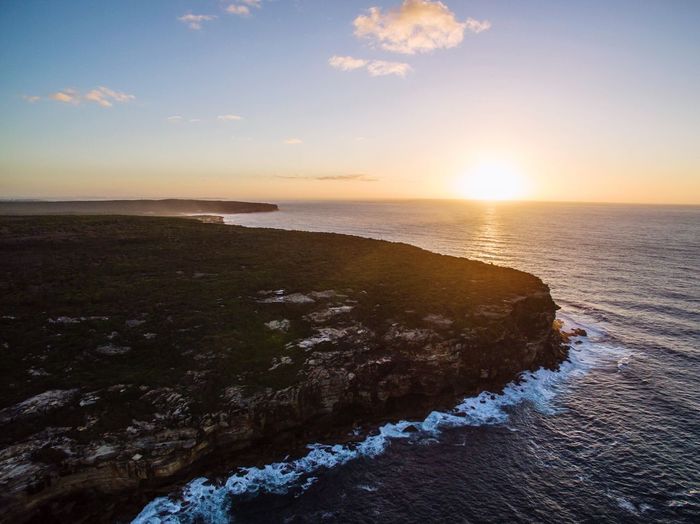 Scenic view of cliff by sea against sky during sunrise at royal national park