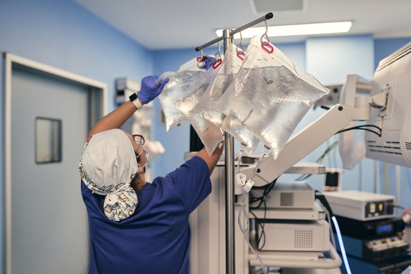 Male doctor removing iv drip bag while standing by monitoring machine in operating room