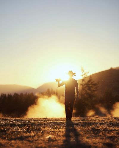 Man holding rifle standing on field against sky during sunset