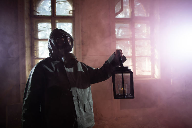 Woman holding oil lamp wearing gas mask standing amidst smoke