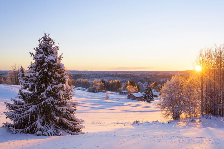 Scenic view of snow covered landscape against clear sky during sunset
