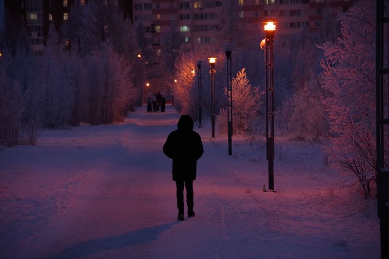 Rear view of man on snow covered street at night