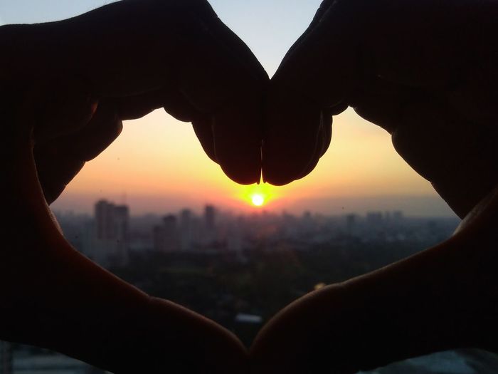 Cropped image of hand holding heart shape against sky during sunset