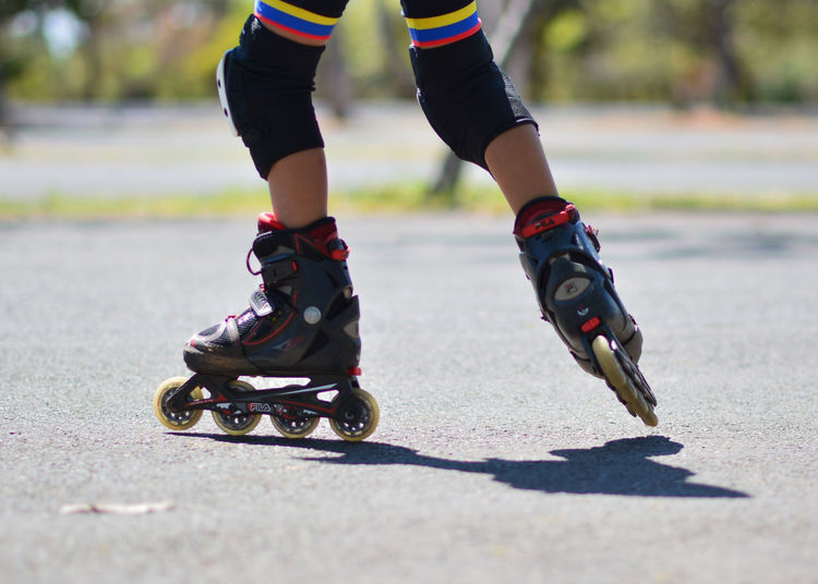 Low section of boy inline skating on road during summer