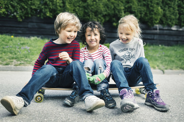 Playful friends sitting on skateboard at yard
