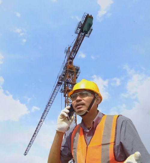 Low angle view of man holding crane against sky