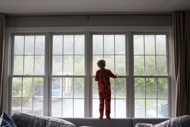 Rear view of boy looking through window at home
