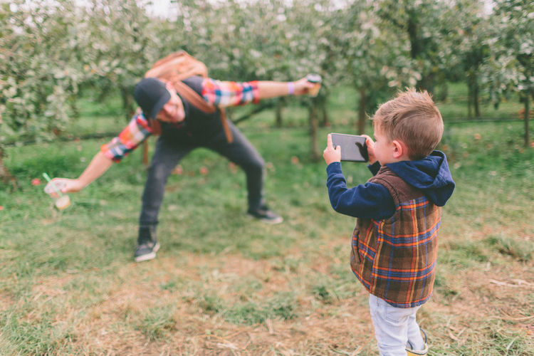 Son photographing father with mobile phone at orchard